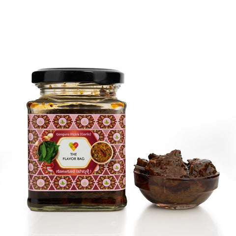 The Flavor Bag Gongura Pickle (Garlic) in a glass jar with a small bowl of chutney. Traditional South Indian condiment.