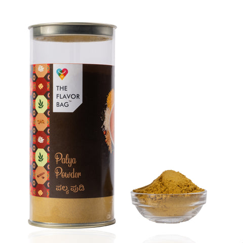 The Flavor Bag Palya Powder seasoning blend in a clear cylindrical container with a small bowl of spice powder.