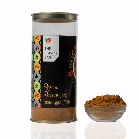 The Flavor Bag TN style rasam powder in a clear cylindrical container with a small bowl of spice blend beside it.