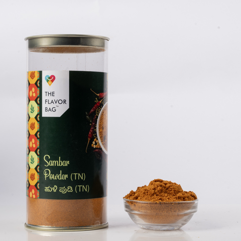 The Flavor Bag Tamil Nadu style sambar powder in a clear cylindrical container with a small bowl of spice blend
